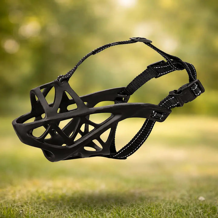 Black silicone basket muzzle with black reflective-stitched straps and side-release buckle against a blurred grassy background.