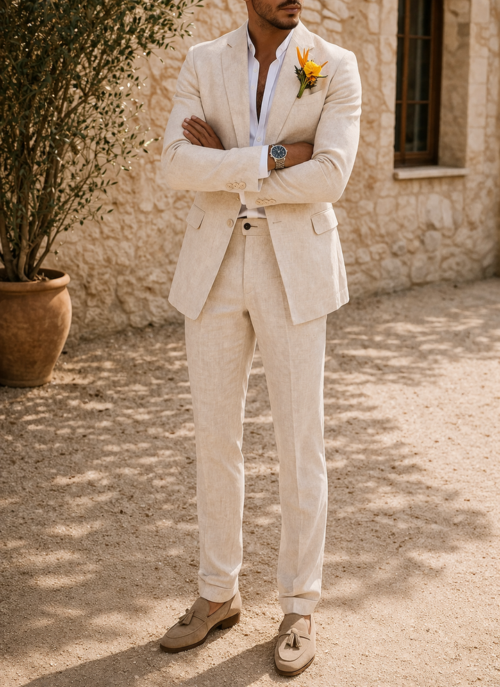 Model in the cream beige suit with arms crossed, a boutonniere on the lapel and tan tasseled loafers.