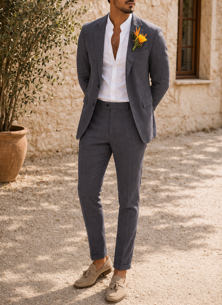 Model in the charcoal gray suit with cuffed trousers, hands behind his back, wearing a white shirt and suede loafers.