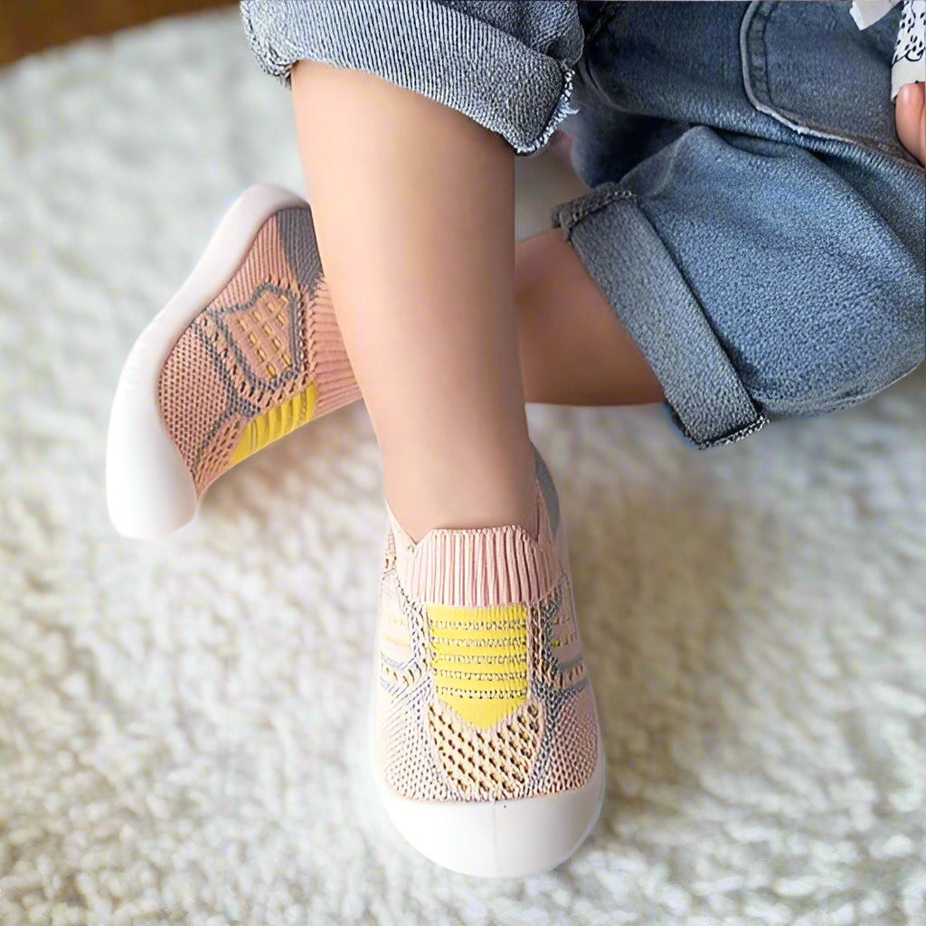 Pink knit baby shoes with yellow stripes, mesh panels and white soles, detail.