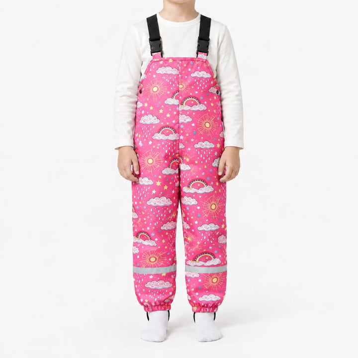 Child wearing hot pink dungarees printed with clouds, raindrops, rainbows, suns and stars, with black buckled straps and reflective ankle bands. 10