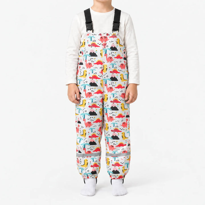 Child wearing white dungarees with a grid background, printed with red and yellow dinosaurs, volcanoes and palm trees, plus reflective ankle bands. 11