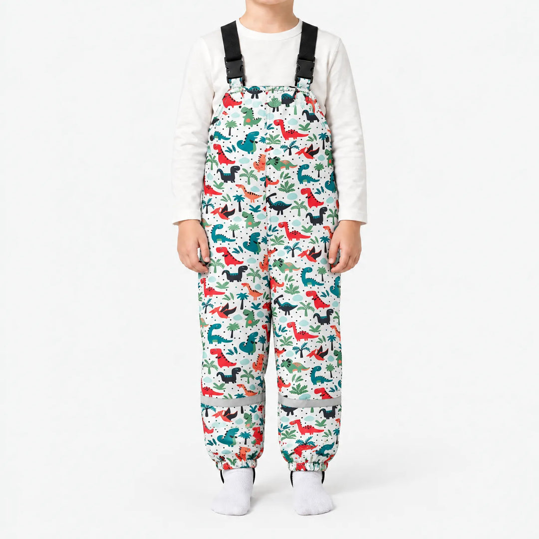 Child wearing white dungarees printed with red, teal and black dinosaurs among palm trees, with elasticated ankles and a reflective band on each leg. 12