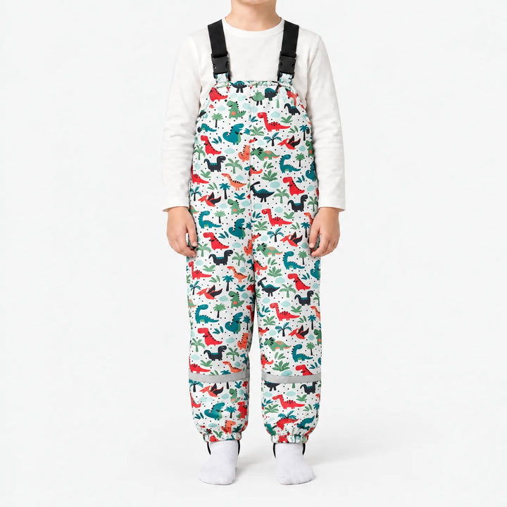 Child wearing white dungarees printed with red, teal and black dinosaurs among palm trees, with elasticated ankles and a reflective band on each leg. 12