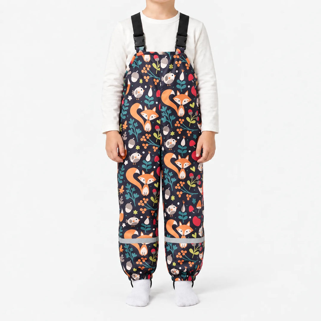 Child wearing dark navy dungarees printed with orange foxes, birds, acorns, berries and leaves, with black buckled straps and reflective ankle bands. 13