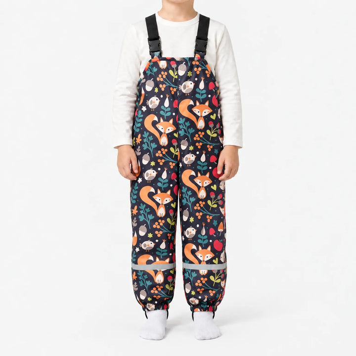 Child wearing dark navy dungarees printed with orange foxes, birds, acorns, berries and leaves, with black buckled straps and reflective ankle bands. 13