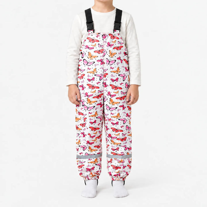 Child wearing white dungarees covered in pink, red and orange butterflies, with black buckled straps, side snaps and reflective ankle bands. 14