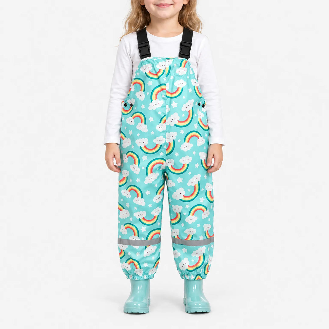 Smiling girl wearing turquoise dungarees printed with smiling cloud rainbows and stars, with matching boots and a reflective band at each ankle. 2