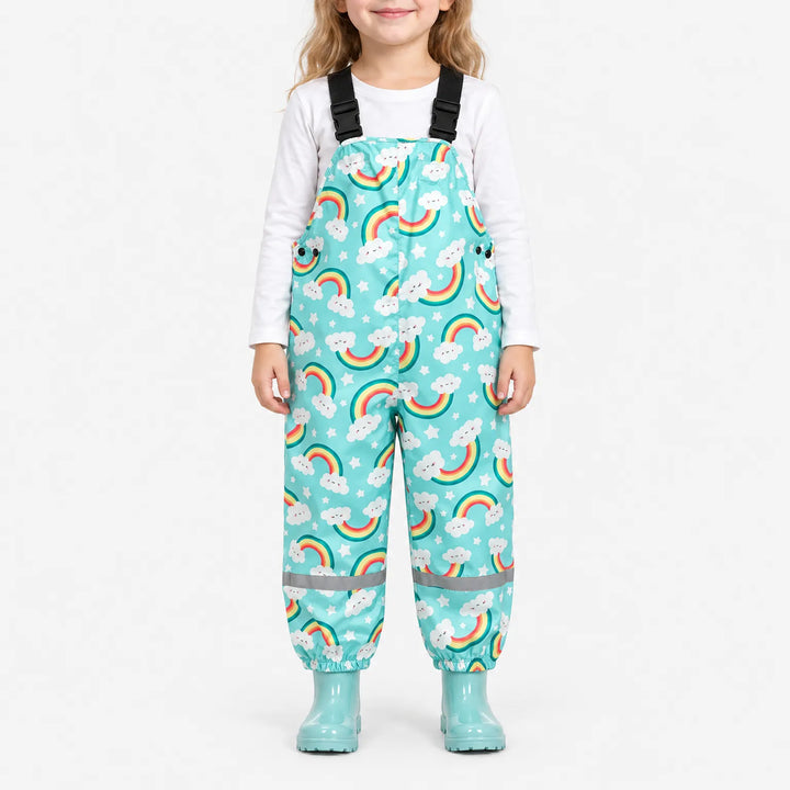 Smiling girl wearing turquoise dungarees printed with smiling cloud rainbows and stars, with matching boots and a reflective band at each ankle. 2