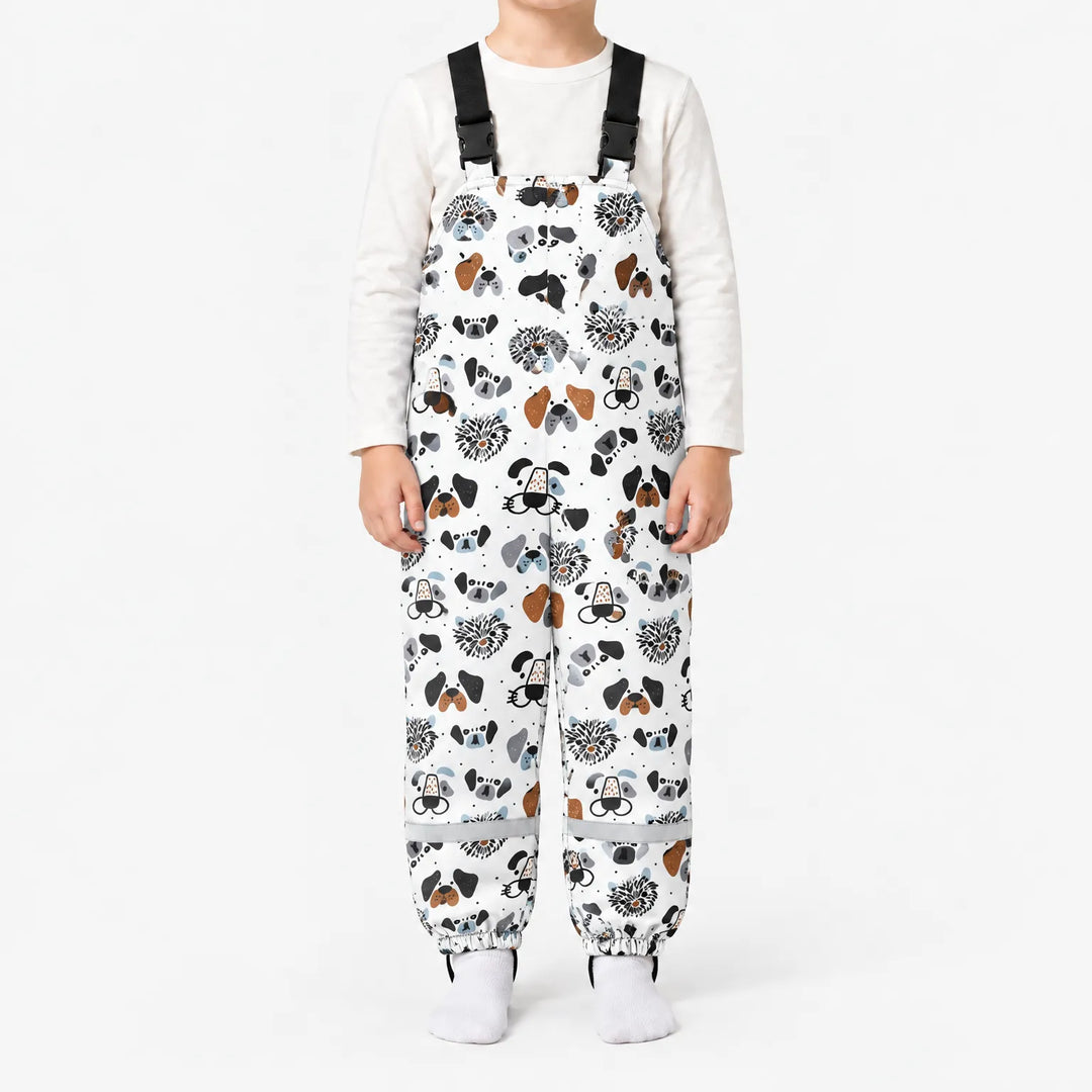 Child standing in white dungarees printed with illustrated dog faces in black, gray and brown, with black buckled straps and elasticated ankles. 7