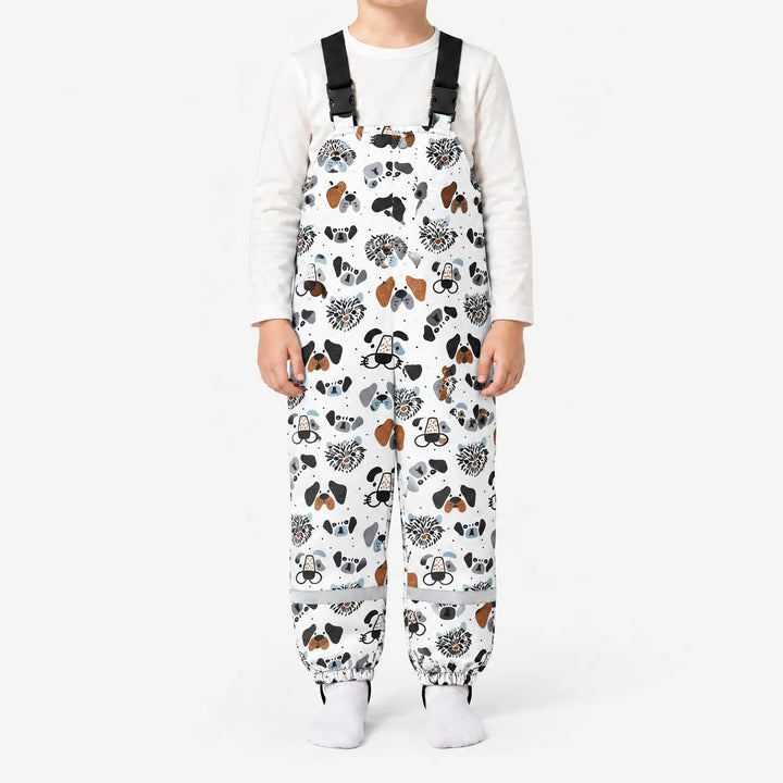 Child standing in white dungarees printed with illustrated dog faces in black, gray and brown, with black buckled straps and elasticated ankles. 7