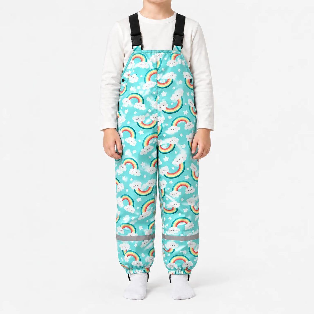 Child standing in turquoise dungarees printed with smiling cloud rainbows and stars, with side snap buttons and a reflective band on each leg. 8
