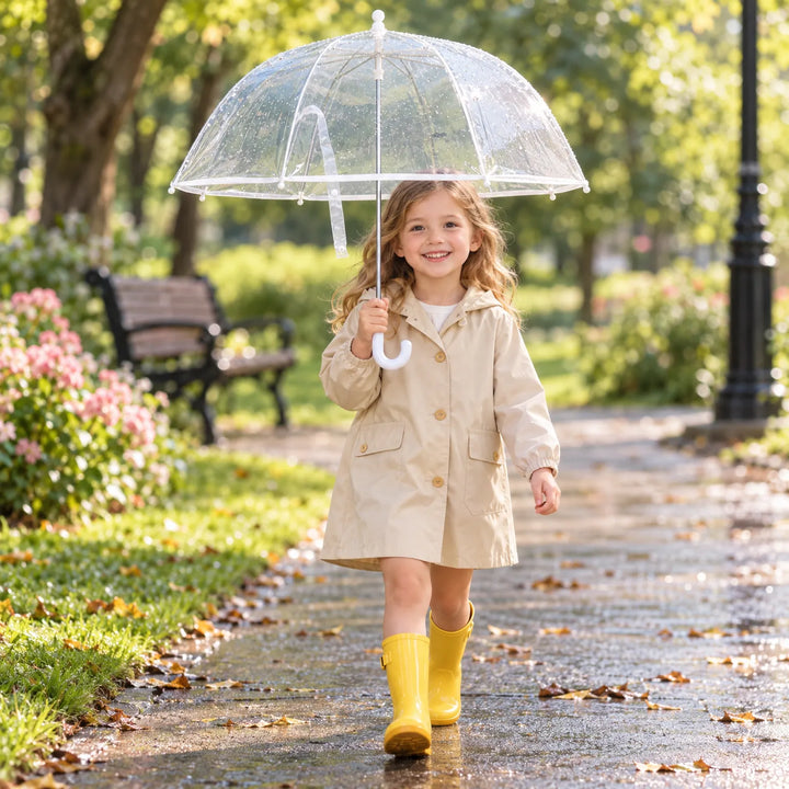Girl in a beige raincoat and yellow rain boots walks along a wet park path holding the clear umbrella. 3