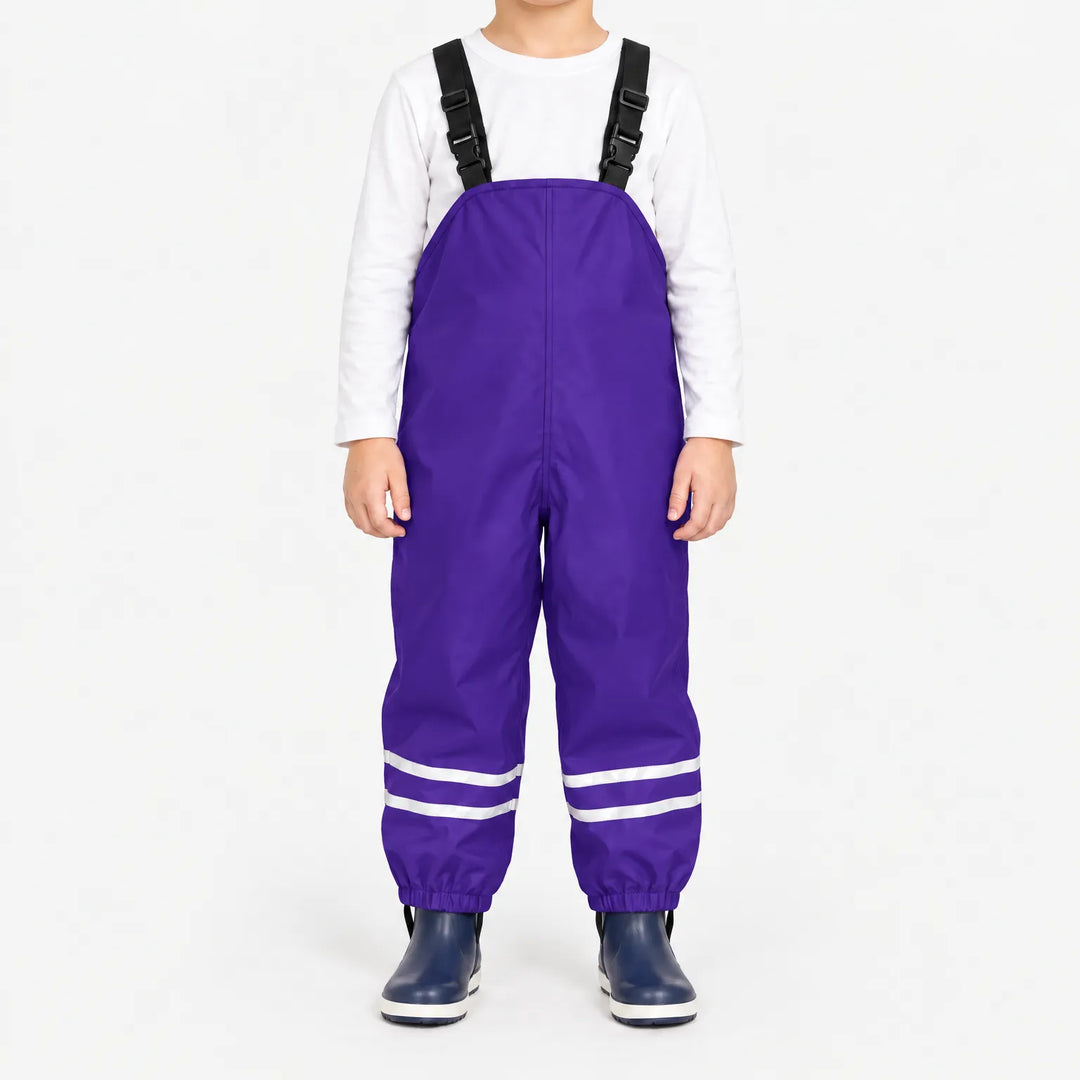 Front view of child wearing purple waterproof overalls with black buckled straps, reflective ankle stripes and elastic cuffs, with navy rain boots. 12