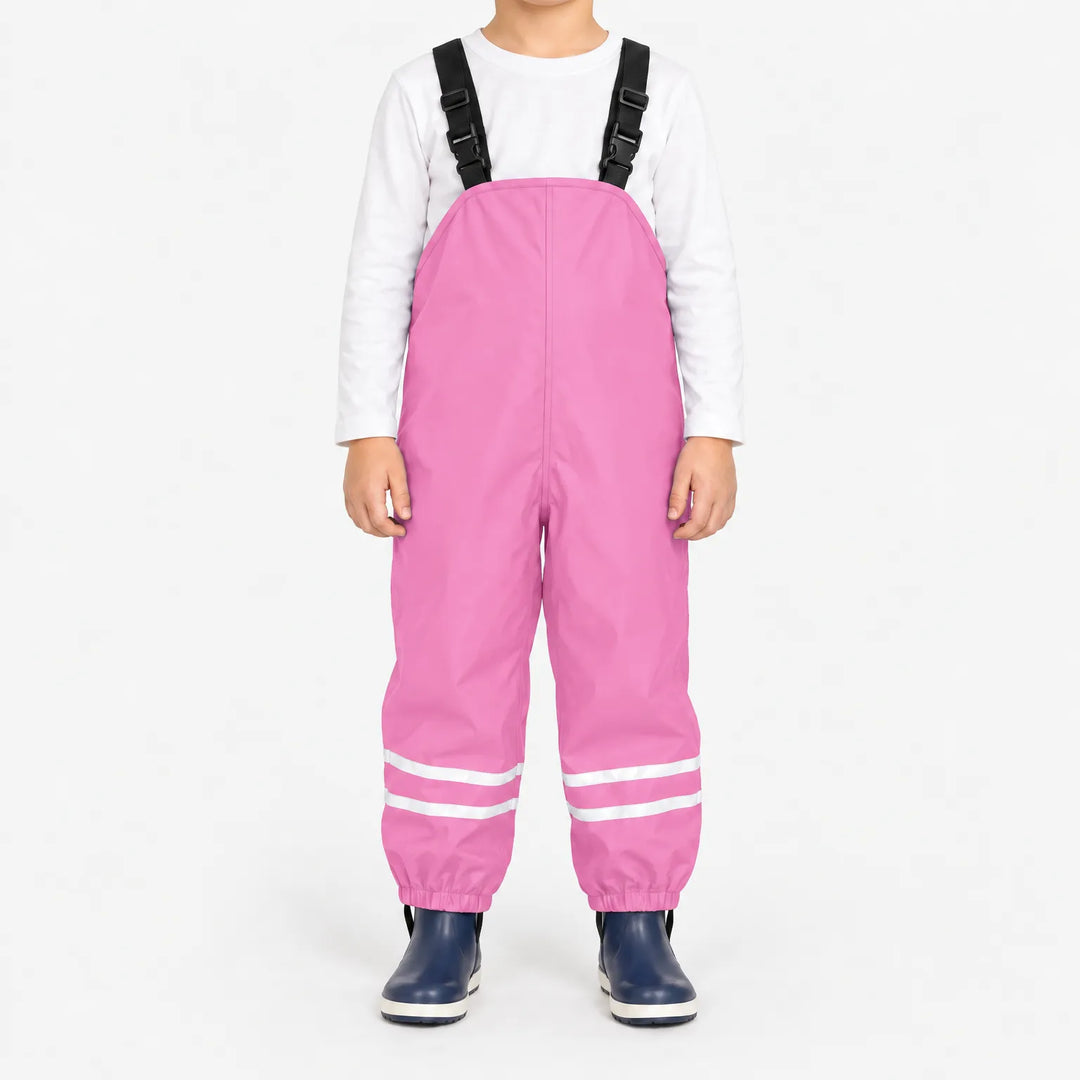 Front view of child wearing light pink waterproof overalls with black buckled straps and reflective ankle stripes, with navy rain boots. 13
