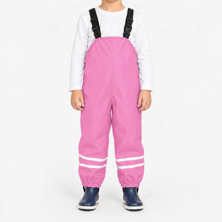 Front view of child wearing light pink waterproof overalls with black buckled straps and reflective ankle stripes, with navy rain boots. 13