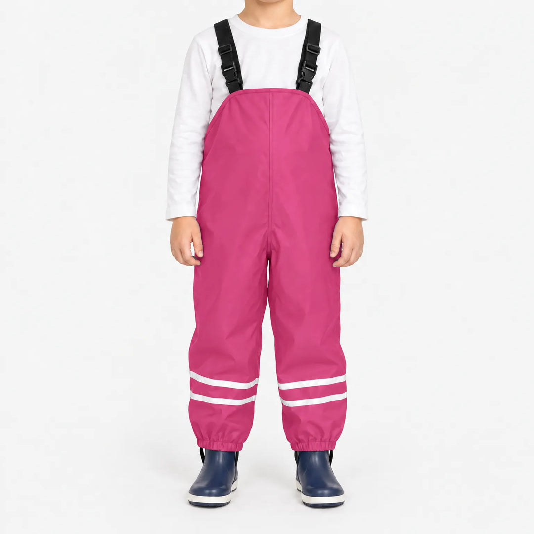Front view of child wearing bright pink waterproof overalls with black buckled straps and reflective ankle stripes, with navy rain boots. 9