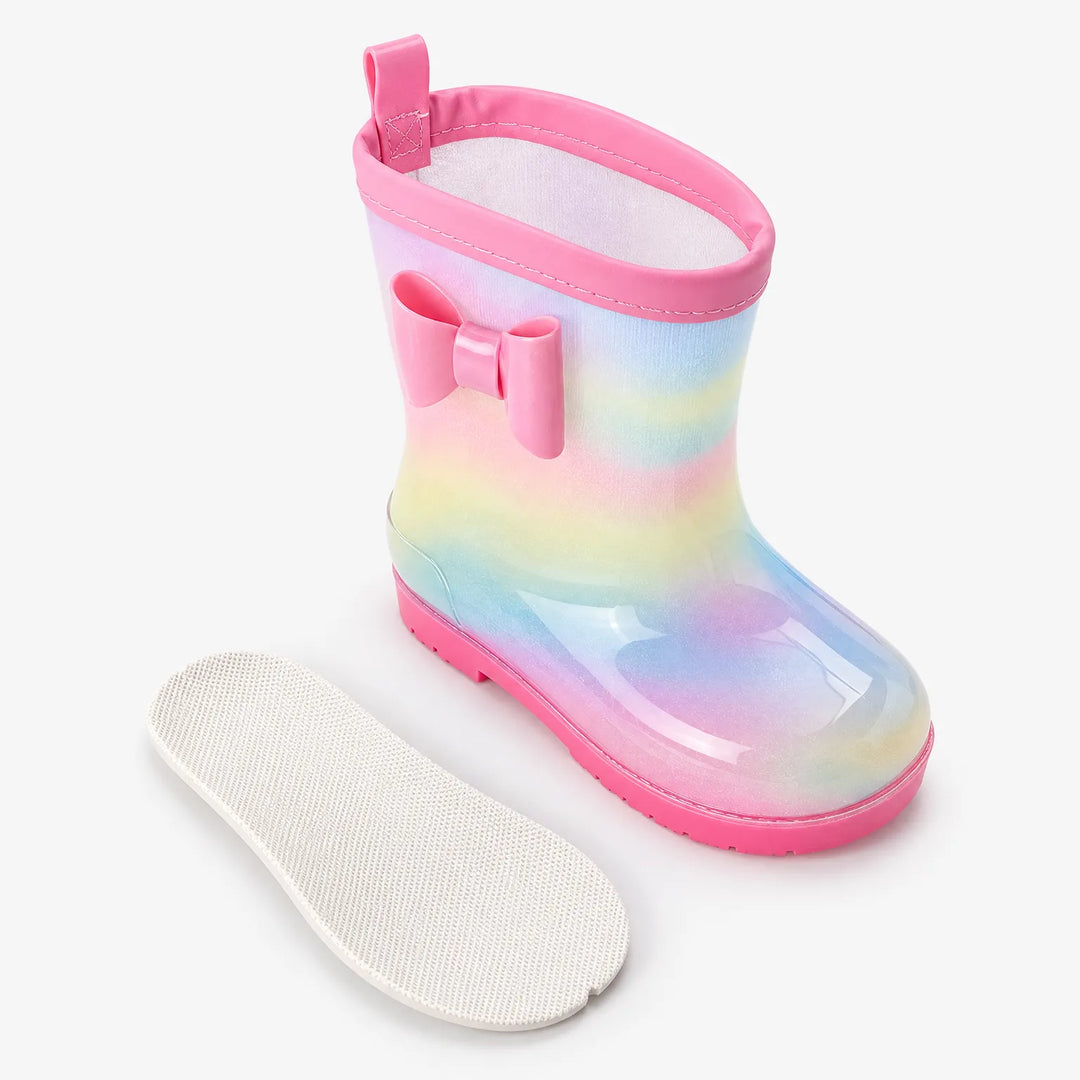 Rainbow rain boot with pink bow and pink trim beside its removable white textured insole, shown from above. 4
