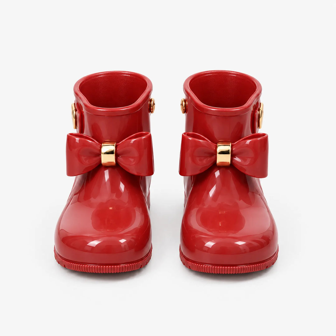 Pair of glossy red rain boots seen from the front on a white background, each with a bow and gold ring. 2