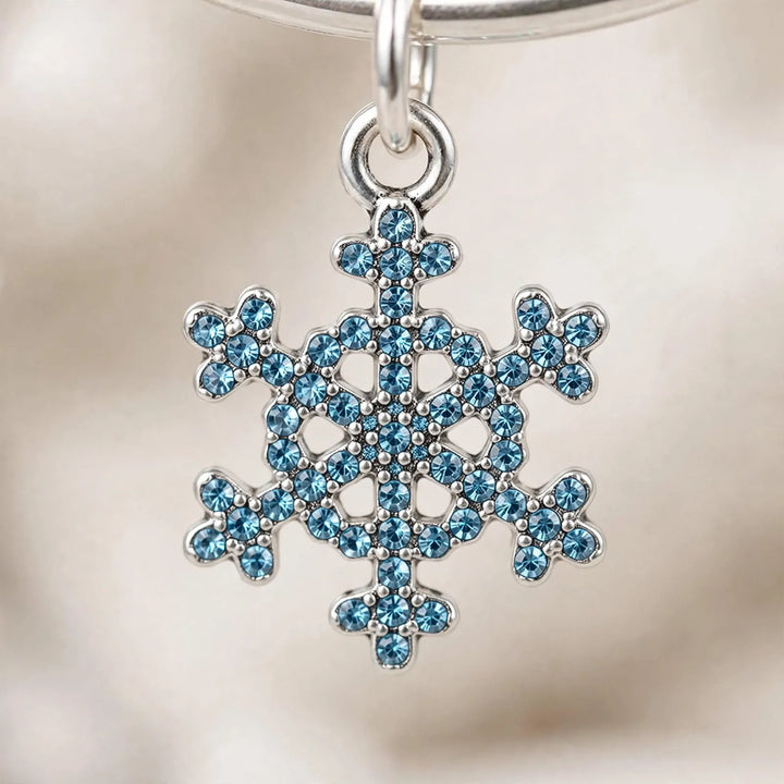 Close-up of a silver snowflake charm set with small blue crystals, hanging from a bracelet 3