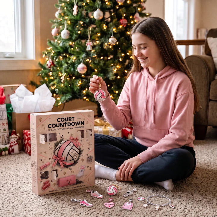 Smiling girl in a pink hoodie holds a volleyball charm beside the advent box and scattered charms 1
