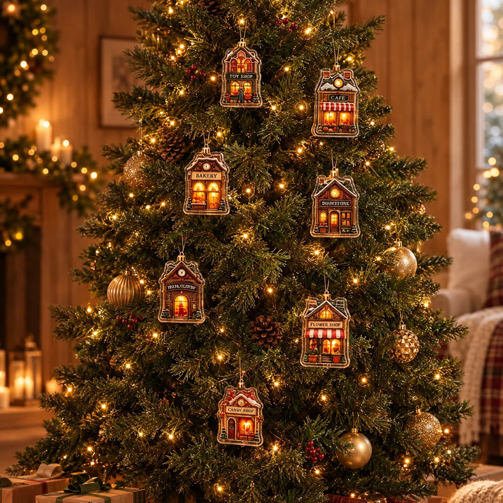 Seven small village-shop ornaments in clear acrylic hang from a lit evergreen tree among gold baubles, pinecones and red berries. 1