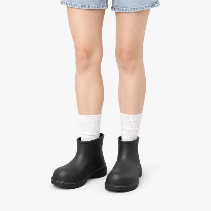 Black ankle boots on a model in white ribbed socks and denim shorts against a plain white background. 2
