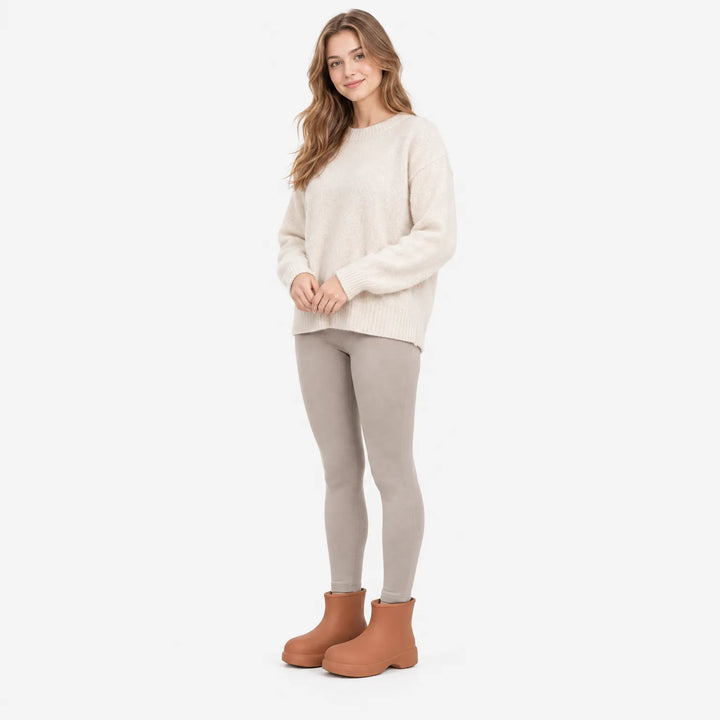 Full-length shot of a smiling model in a cream sweater and gray leggings wearing terracotta-brown ankle boots. 4