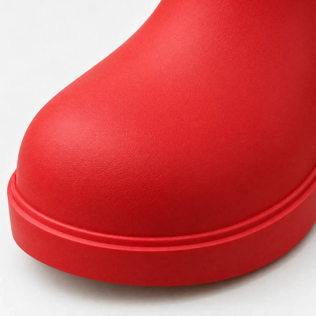 Close-up of a red boot's rounded toe and chunky sole edge, showing the matte textured rubber surface. 6