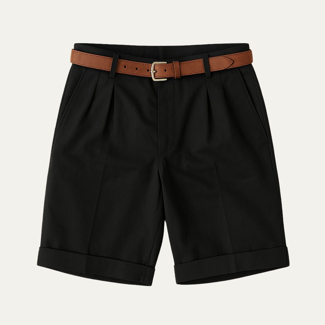 Flat lay of black double-pleated shorts with turn-up hems and a tan leather belt with gold-tone buckle.