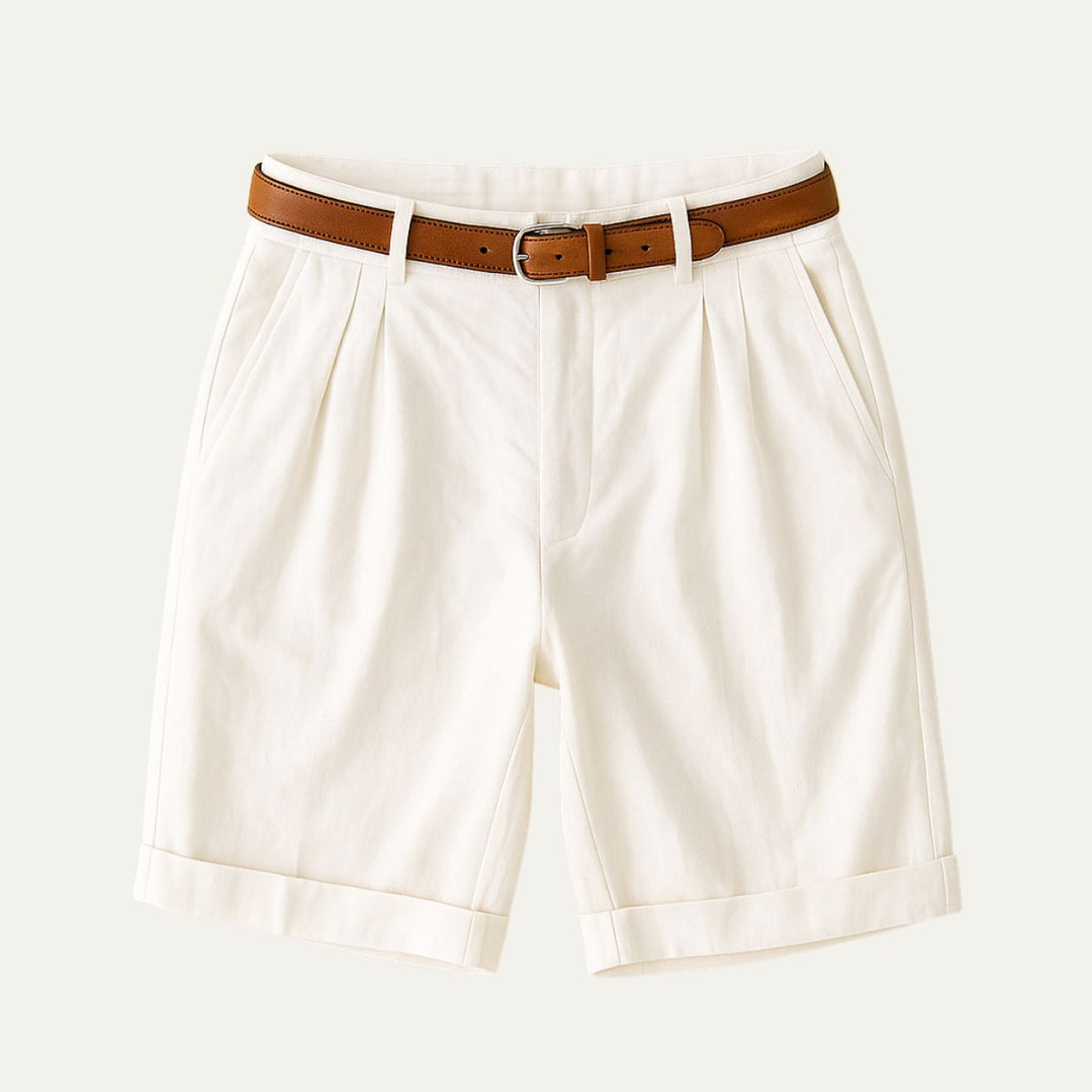 Flat lay of cream double-pleated shorts with turn-up hems and a tan leather belt with silver buckle.