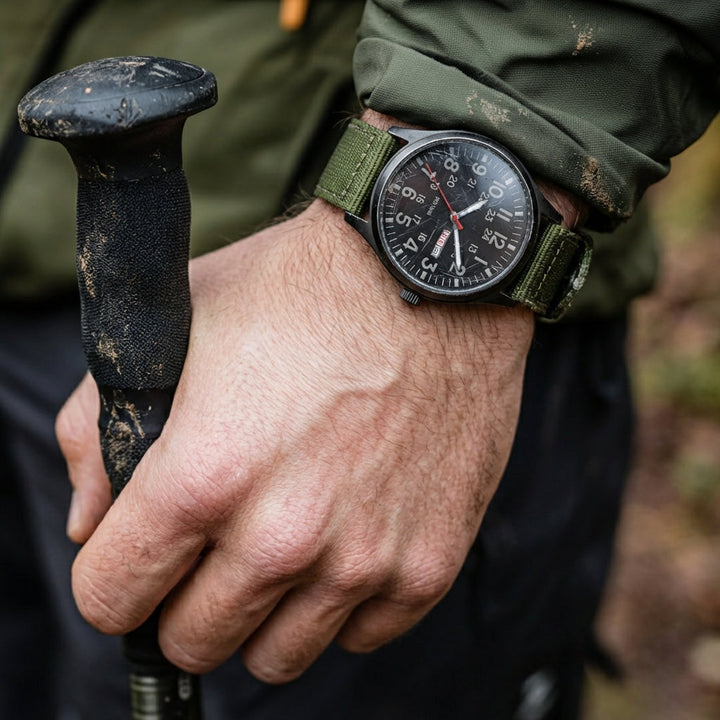 Men's field watch with a woven fabric strap on a hiker's wrist, close-up detail.