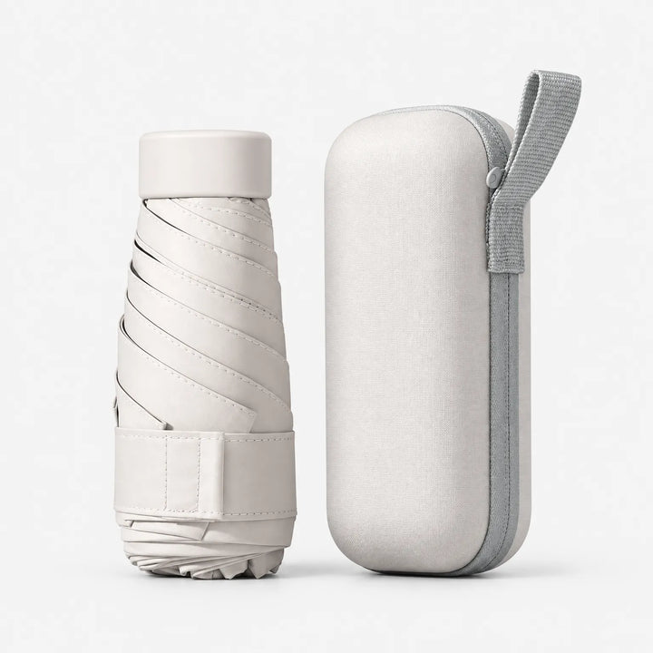 Folded cream umbrella with strap and cap next to its matching cream hard case with a gray zipper and carrying loop. 6