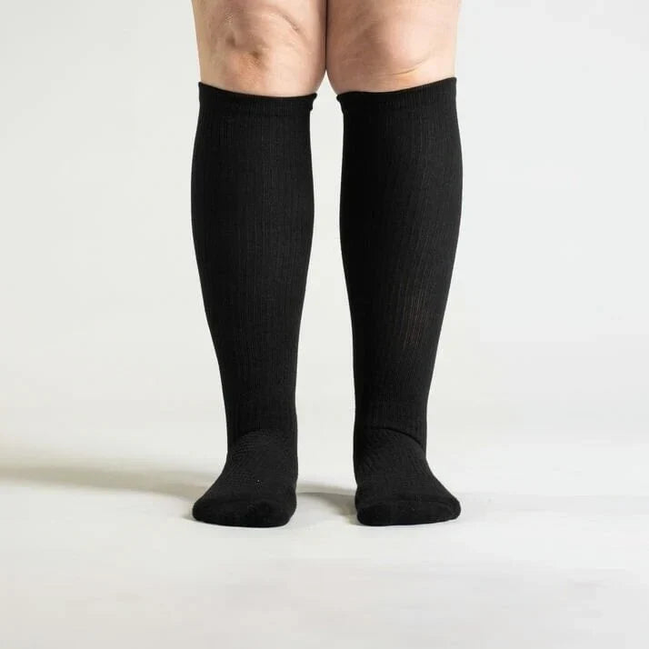 Front view of a model standing in black knee-high ribbed socks that end just below the knees. 3