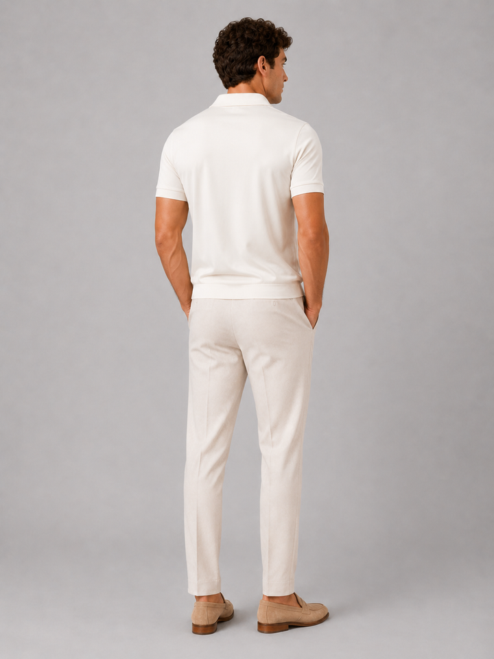 Back view of a model in the cream polo, showing the plain back and ribbed hem, with light trousers and tan loafers. 24