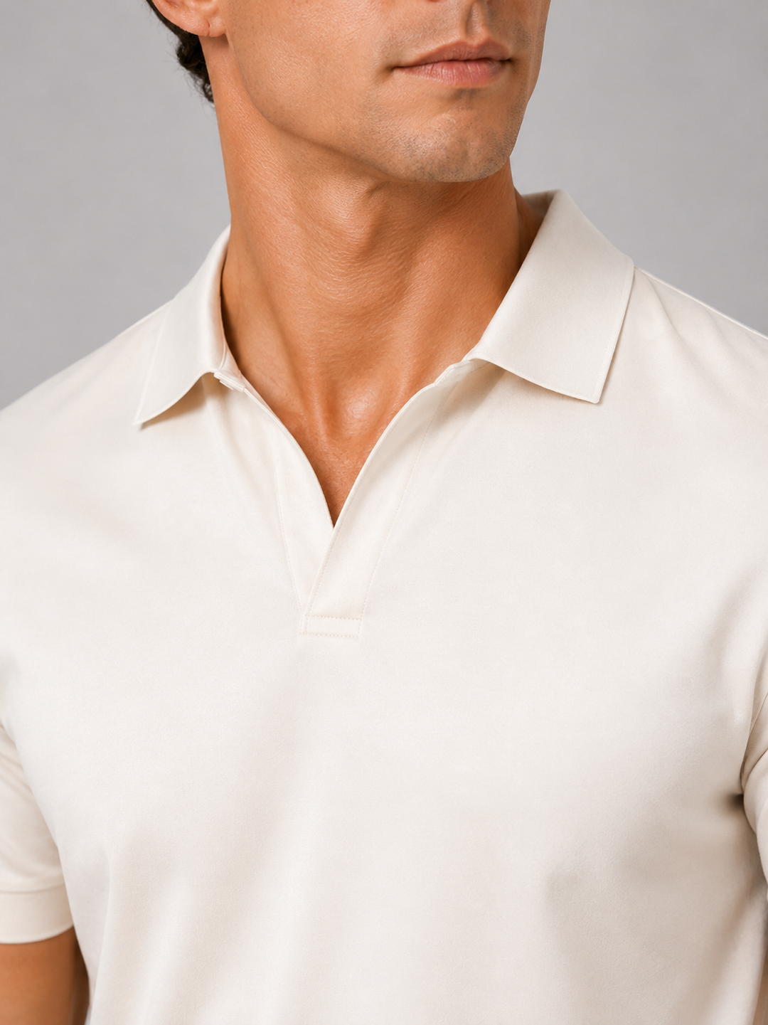 Close-up of the cream polo's open johnny collar and stitched placket, showing the smooth, soft-looking fabric on a model's neck and chest. 22