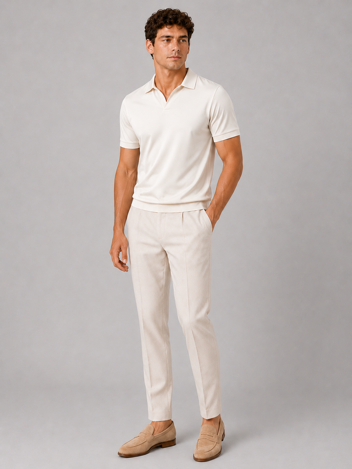 Full-length front view of a model wearing the cream polo with light trousers and tan suede loafers against a gray backdrop. 23