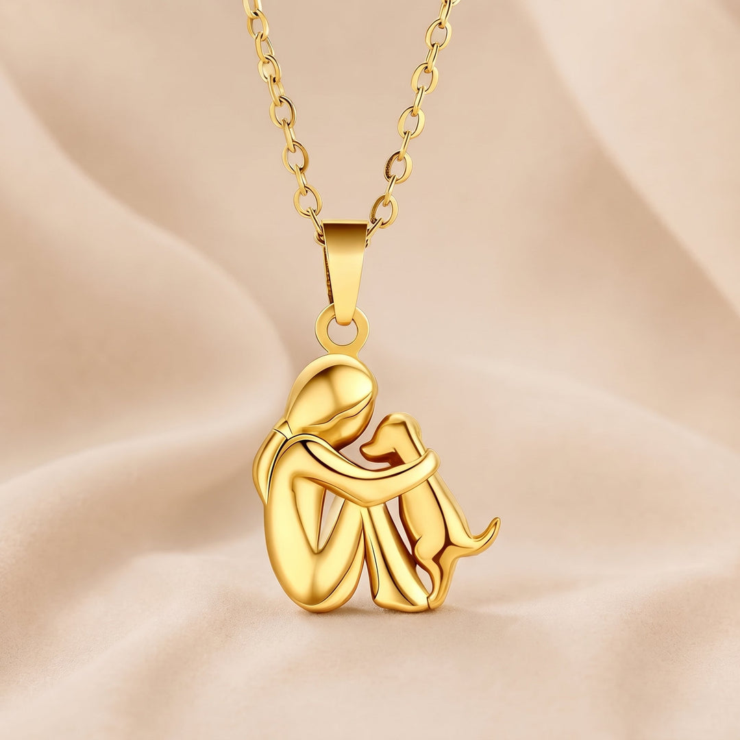 All gold-tone pendant of a seated figure embracing a small dog, hanging from a matching gold-tone chain on soft fabric. 5