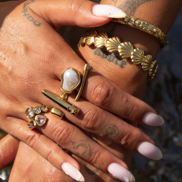 Axis adjustable sculptural gold ring worn with stacked rings and gold bracelets.
