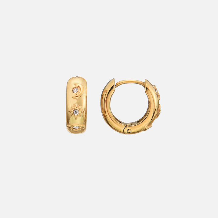 Pair of chunky gold huggie hoops on a light background, one showing the moon, star and eye motifs with tiny clear stones, the other showing the hinge. 1