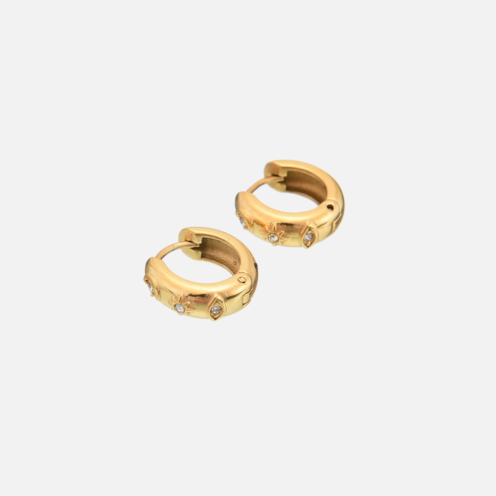 Two gold huggie hoops seen at an angle on a plain light background, showing the star and eye motifs set with small clear stones. 2