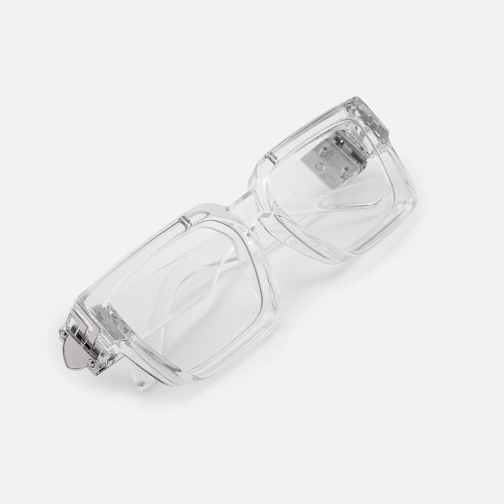 Folded clear rectangular glasses seen at an angle from above, showing the silver metal hinge detail on the thick transparent frame. 22