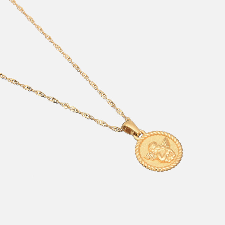 Angled view of the round cherub pendant and twisted gold chain lying flat on a light gray surface. 2