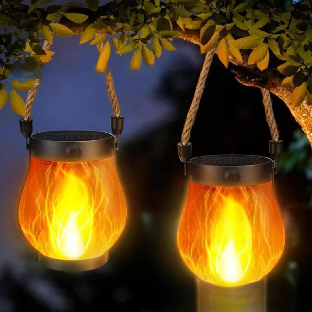 Two lanterns hung by rope handles from a tree branch at night, glowing with orange flames 7