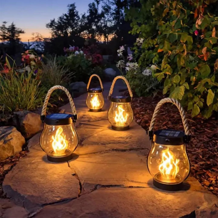 Four lit lanterns placed along a flagstone garden path at dusk among flowers and shrubs 8