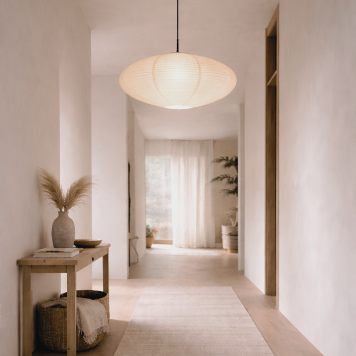 Lit oval paper pendant lamp glowing above a bright hallway with a wooden console, pampas grass vase and woven basket. 2