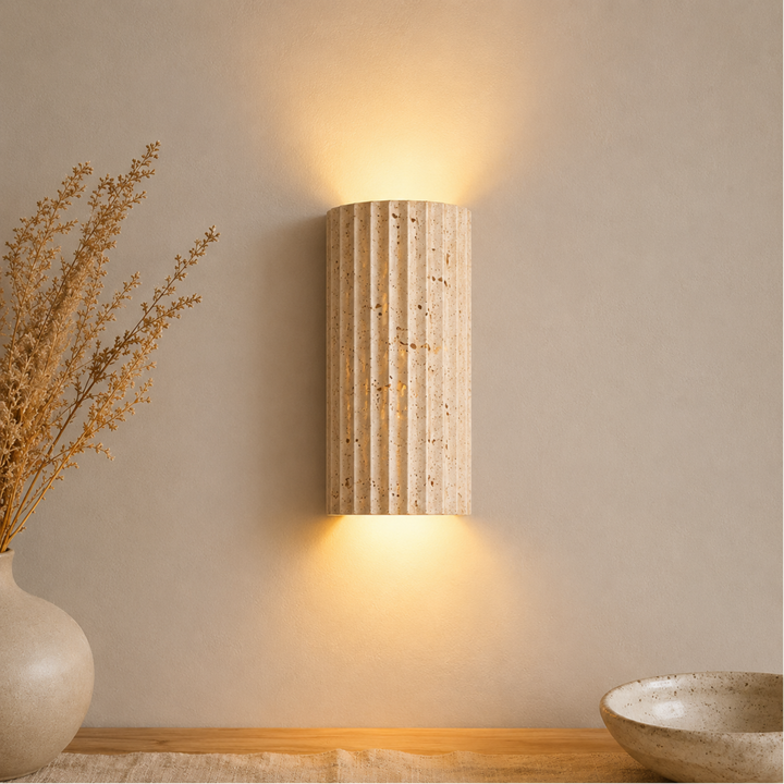 Natural Stone Wall Sconce Wall Light in beige stone, lit from above and below beside dried stems and a ceramic bowl.