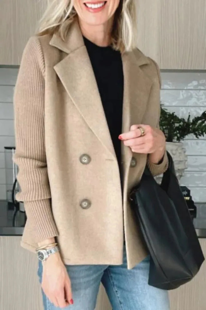 Close-up of the smiling model in the beige jacket, one hand on the lapel, holding a black bag 11