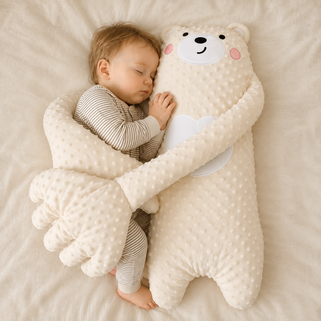 Sleeping baby in striped pajamas nestled against a cream dotted-plush bear whose long arms wrap around the child on a soft bed. 1