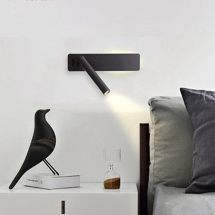 Black wall light detail above a bed with its spot aimed at a nightstand.